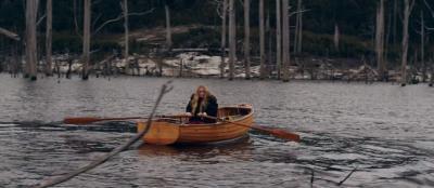 Person rowing a small boat on a lake with trees in the distance