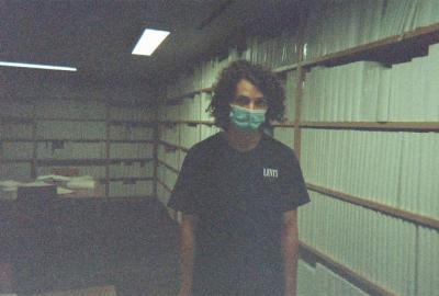 Picture of Joe in mask, black t-shirt in front of the library room at MONA